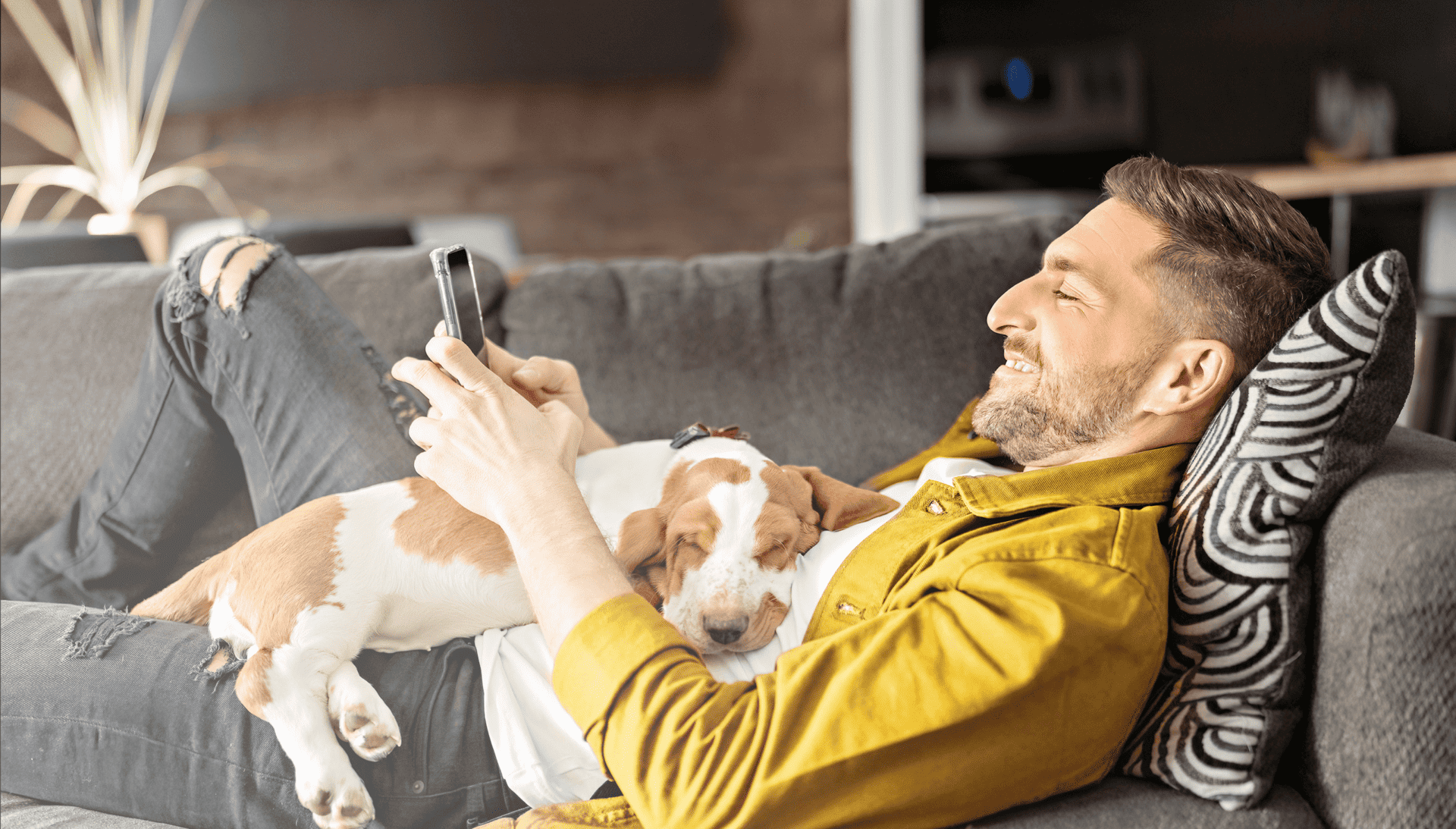 Man lying on couch with a dog and his phone.