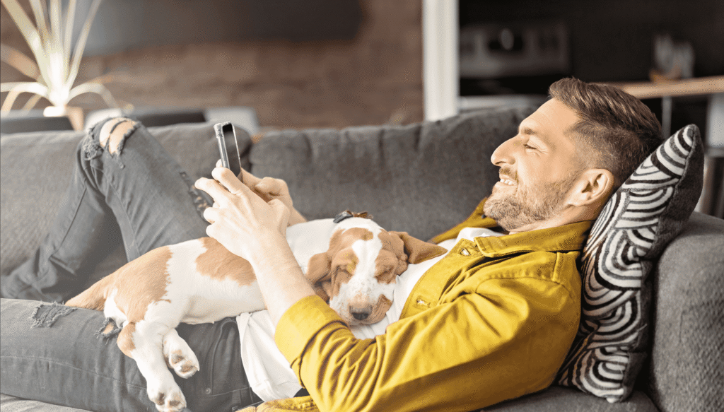 Man lying on couch with a dog and his phone