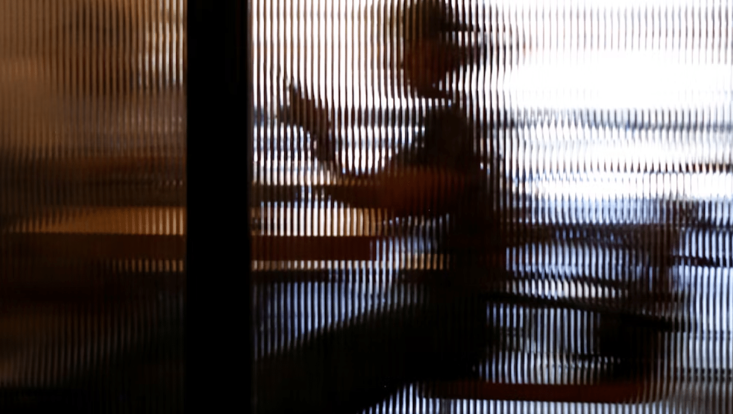 Person, die mit einem Smartphone an einem Tisch sitzt hinter einer unschärfe erzeugenden Glasscheibe