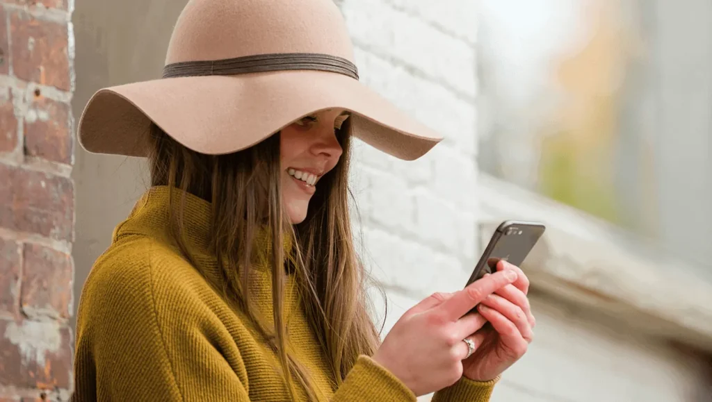 Girl with hat smiling looking at her smartphone