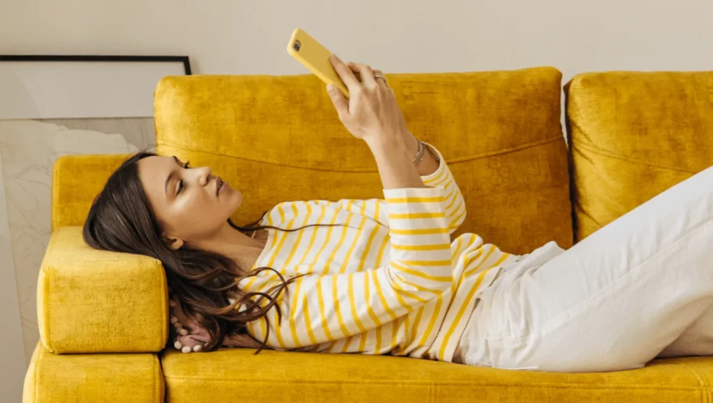 Young woman lying in couch and looking at her smartphone