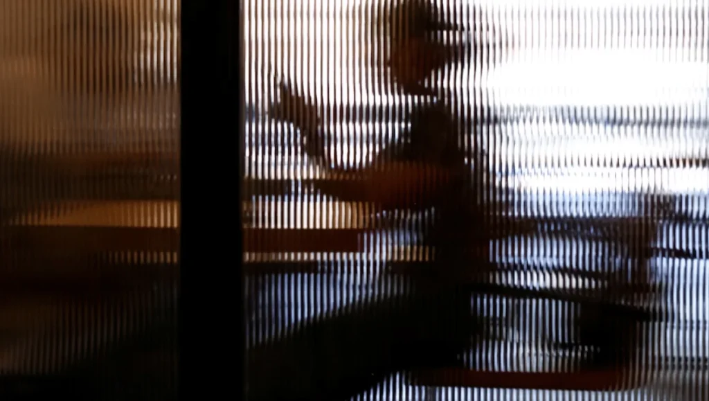 Person, die mit einem Smartphone an einem Tisch sitzt hinter einer unschärfe erzeugenden Glasscheibe