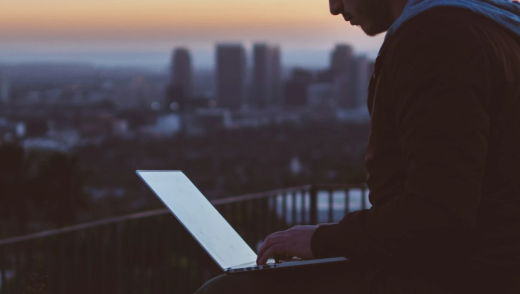 Source of funds hero image, a picture of a man at sunset working on his laptop with a city in the background